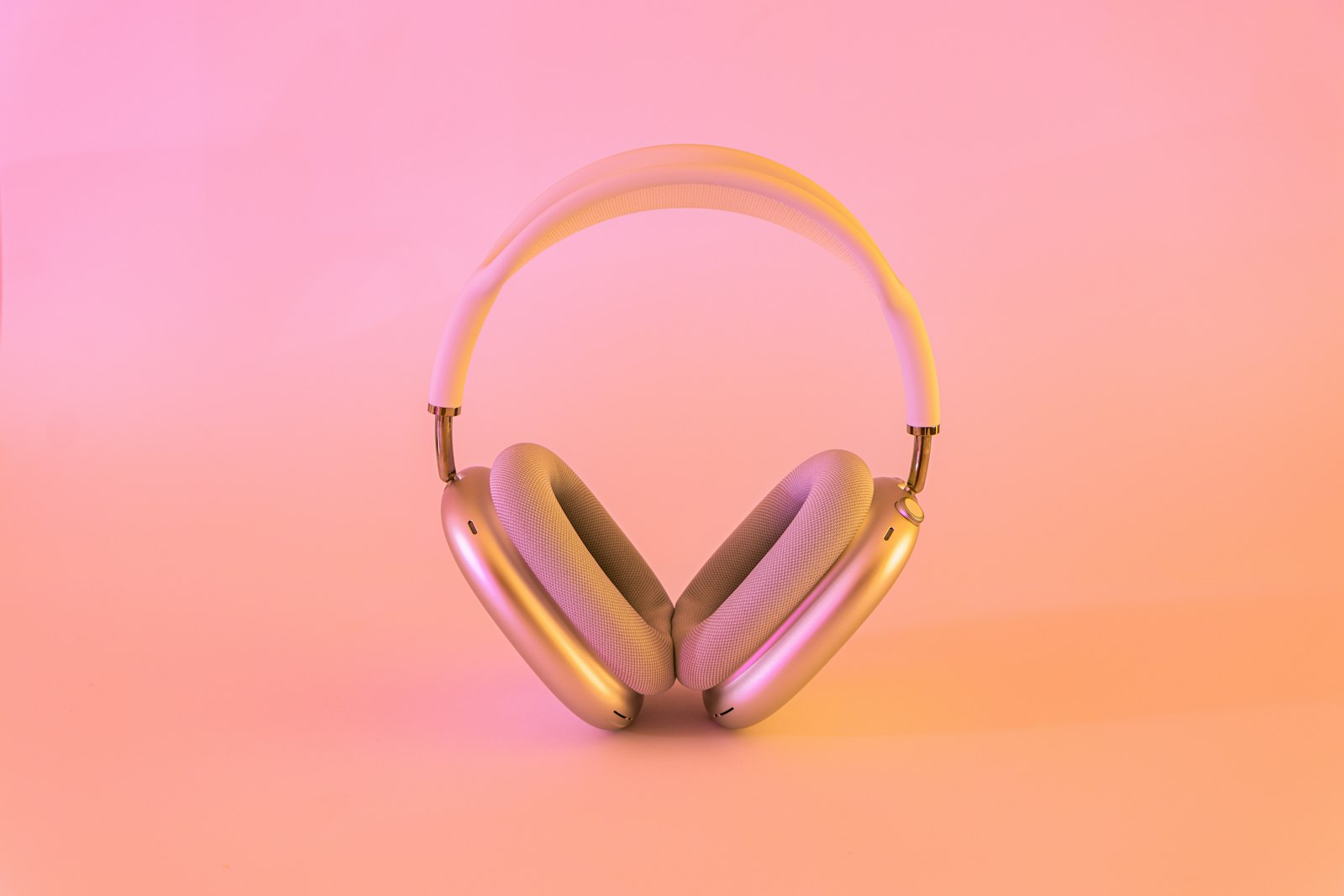 Silver over-ear headphones with light mesh-style pads on a pink background.